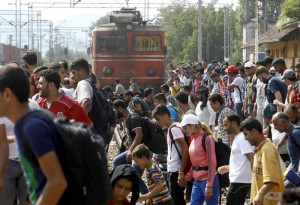 Migrants cross the raiway tracks in front of a train entering the railway station in the southern Macedonian town of Gevgelija, on Saturday, Aug. 15, 2015. (ANSA/AP Photo/Boris Grdanoski)