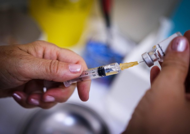 La mano di un dottore impugna una siringa con il vaccino.