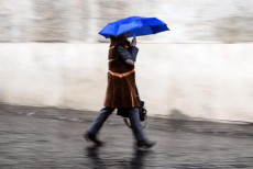 Una persona si ripara con l'ombrello sotto la pioggia in piazza Colonna a Roma.