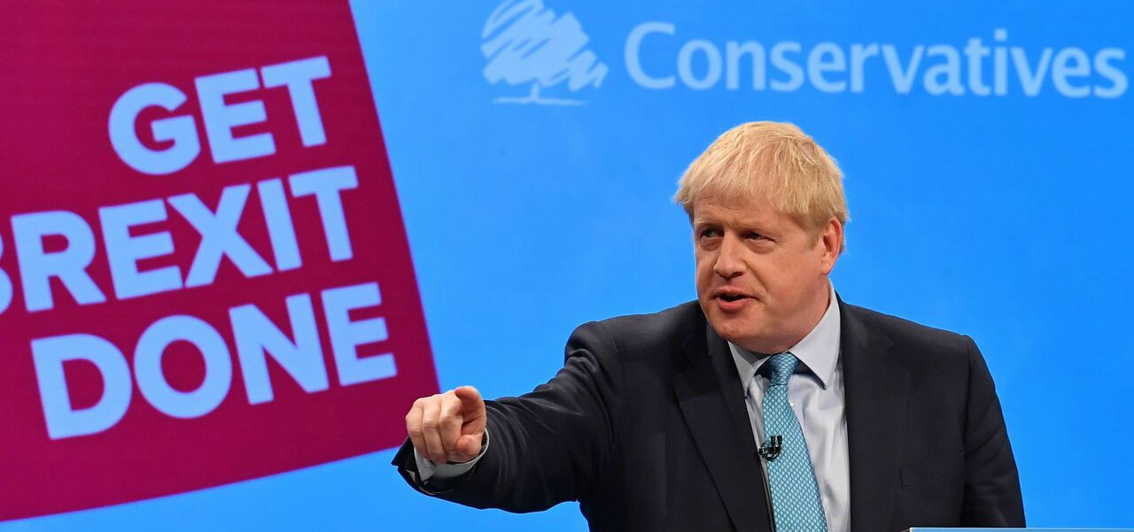 Il premier britannico Boris Johnson pronunica un discorso s Manchester davanti al suo motto di campagna "facciamo il Brexit" per la separazione del Regno Unito dall'Unione Europea, l'anno scorso.