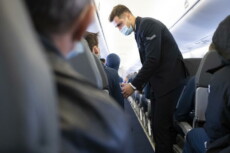 Stewart con la mascherina parla con un passeggero su un aereo in volo.